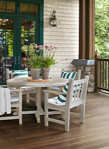 An outdoor living area featuring a wooden deck and ceiling, white brick walls with green trim, and a white table with matching chairs. 