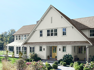 An off‑white painted house with a yellow front door, green bushes and grass in front, and a blue sky overhead.