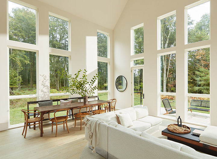 A white painted open concept living room dining room with a vaulted ceiling, lots of windows, and neutral decor.