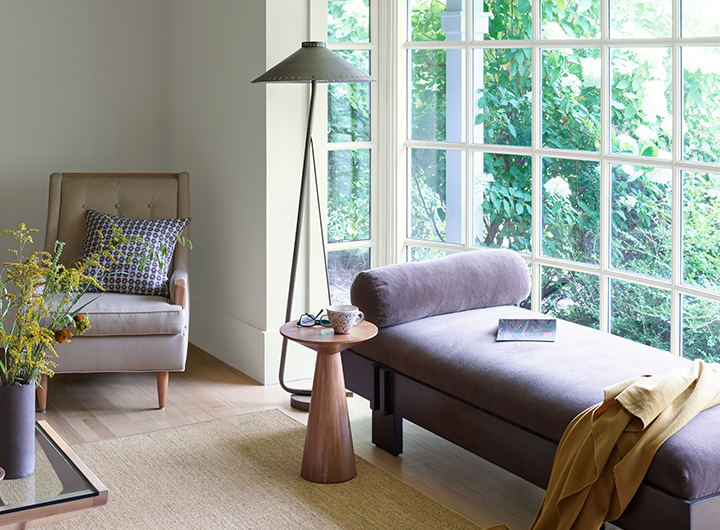A spacious gray painted living room with a purple chaise, floor lamp, and jute rug.